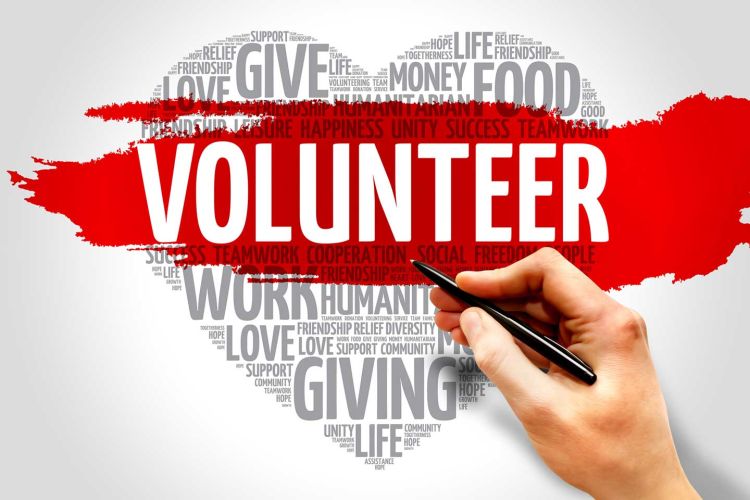 An illustration of a heart shape that is comprised of words all relating to volunteering and charity. In the center with white font and a red background it reads, "VOLUNTEER".