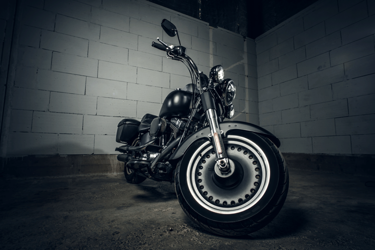 A motorcycle parked in front of a white cinderblock wall. The angle of the photo is from in front of the motorcycle at wheel level.