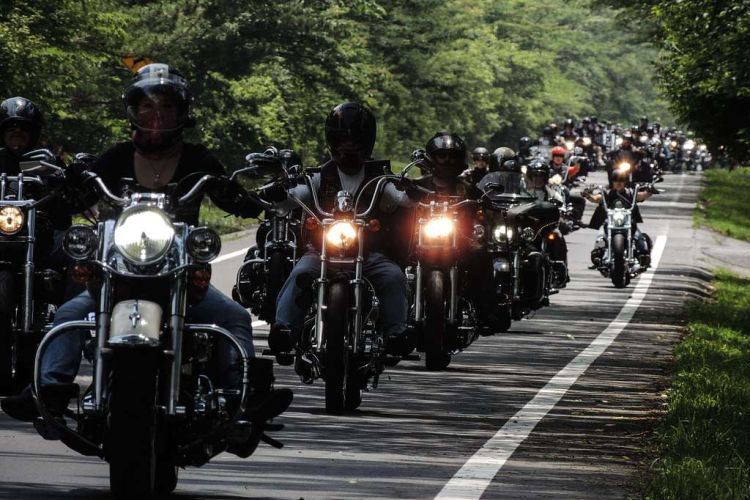 Motorcyclist riding in a line along a two-lane asphalt road.