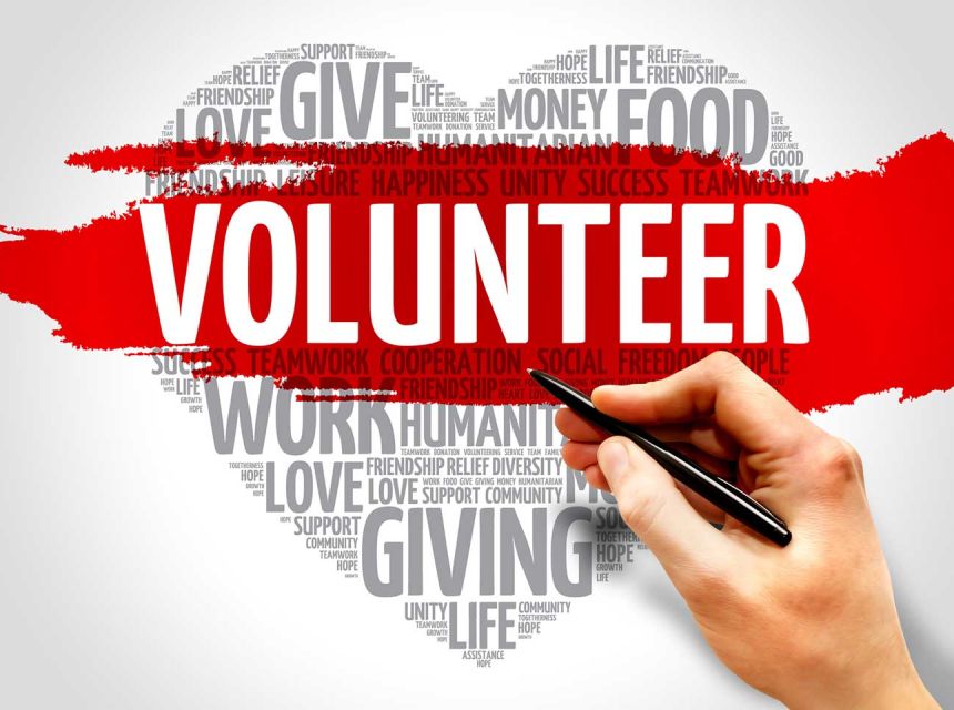 An illustration of a heart shape that is comprised of words all relating to volunteering and charity. In the center with white font and a red background it reads, "VOLUNTEER".