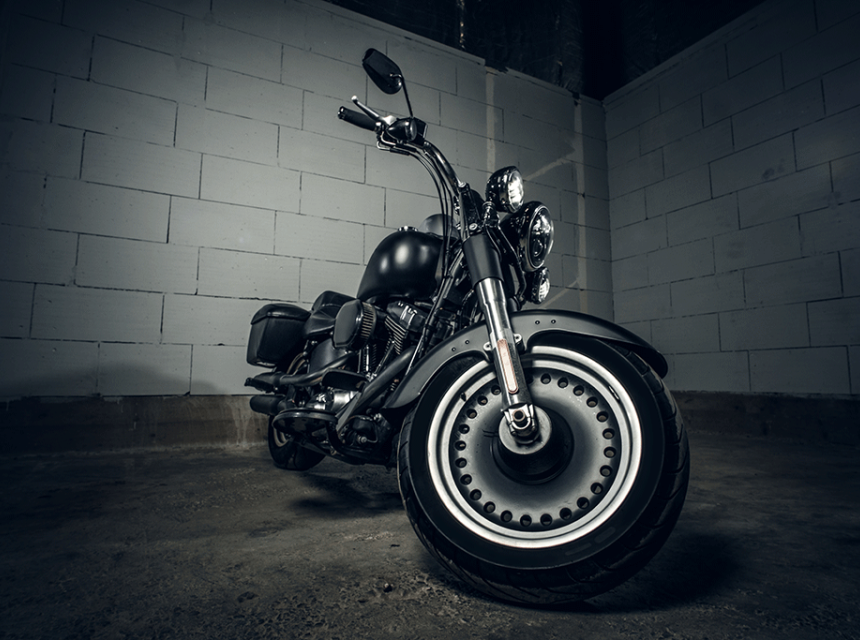 A motorcycle parked in front of a white cinderblock wall. The angle of the photo is from in front of the motorcycle at wheel level.